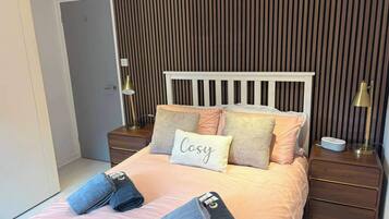 A bedroom with a bed, bedside tables, lamps, and a wall with vertical lines.