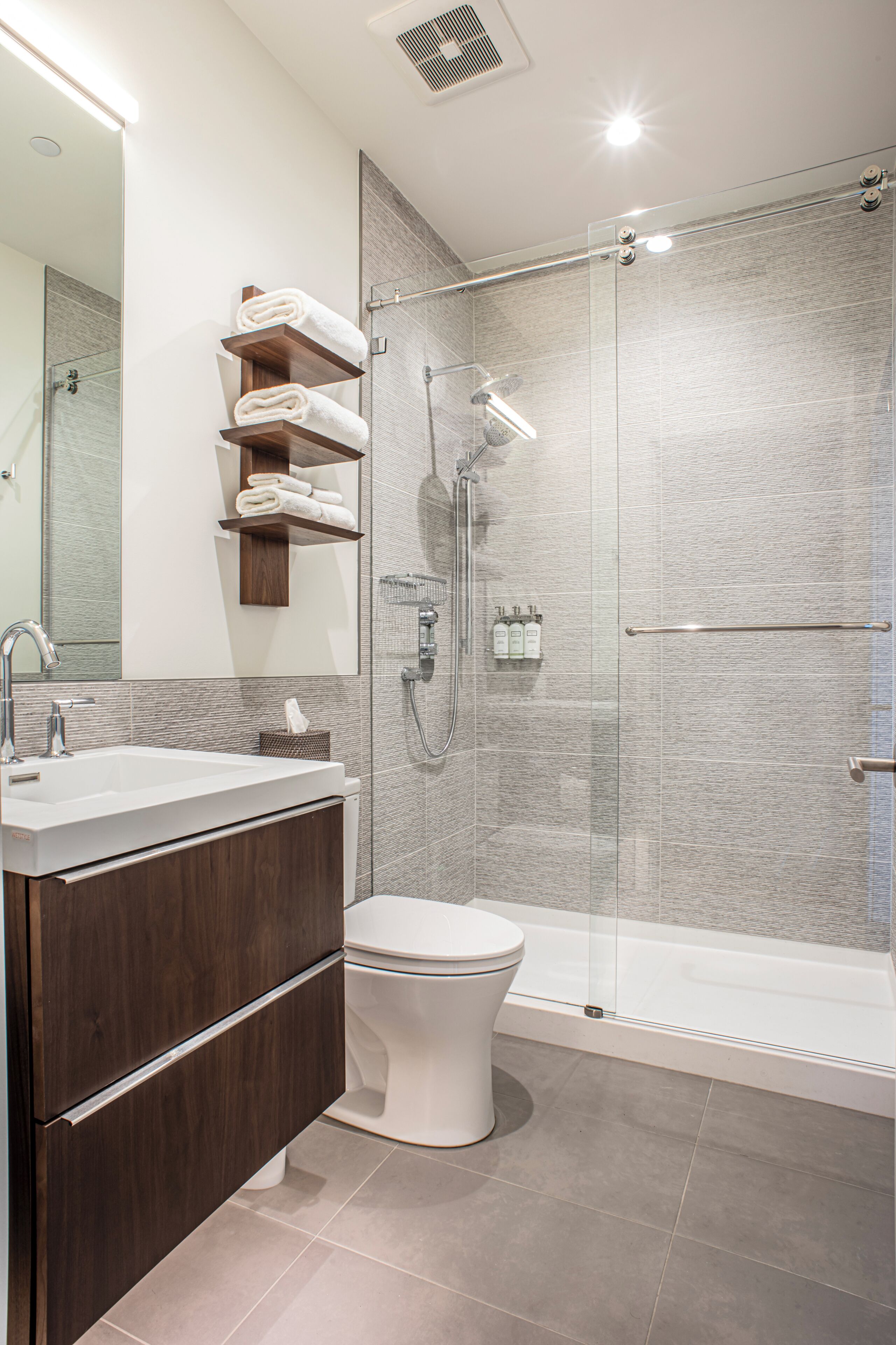 Un bany modern amb un envà de dutxa de vidre, un vàter blanc i un lavabo amb mirall.