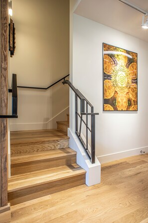 A staircase with wooden steps and a metal handrail, leading to a landing with a wall-mounted artwork. - The Elevation Experience | All 6 Lofts ( up to 31 guests ) (Asheville)