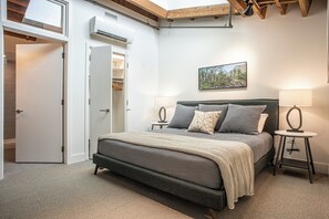 A bedroom with a bed, bedside tables, a lamp, a painting on the wall, and an open closet. - The Elevation Experience | All 6 Lofts ( up to 31 guests ) (Asheville)
