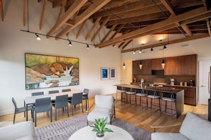 Een moderne keuken met houten balken, een eethoek met een groot schilderij en een bar met krukken.