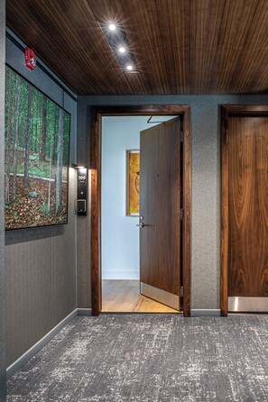 A hallway with a wooden ceiling, a fire alarm, a digital elevator control panel, and a door leading to another room. - The Elevation Experience | All 6 Lofts ( up to 31 guests ) (Asheville)