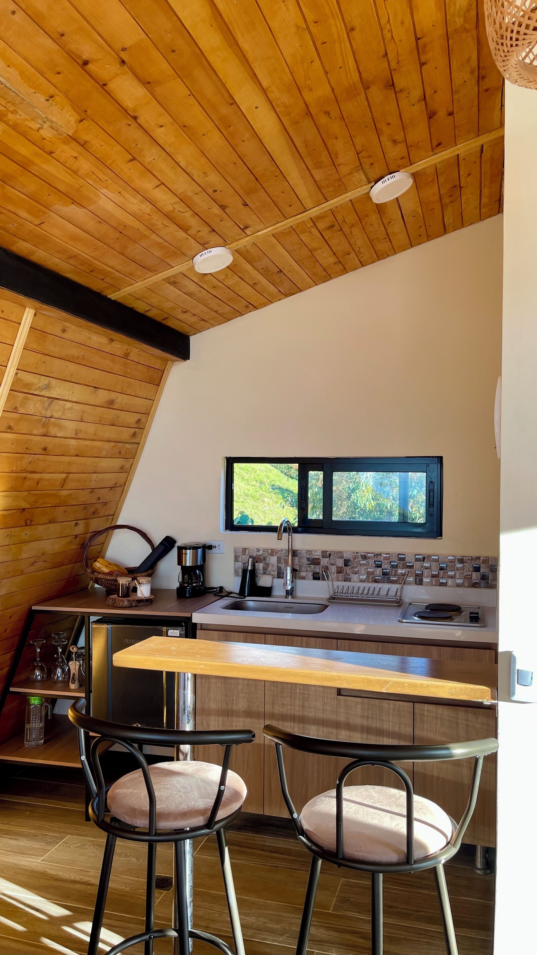 A kitchen with a wooden ceiling, a window, and two bar stools.