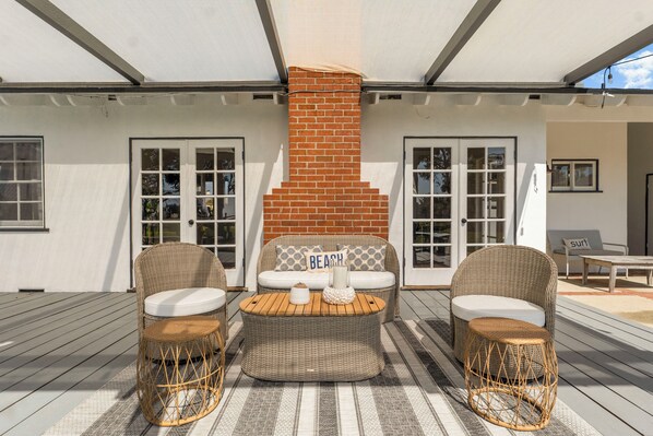 A covered outdoor seating area with wicker furniture and a brick fireplace.