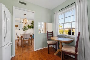 Una cocina con suelo de madera, un comedor con mesa y sillas, y un ventanal con cortinas.