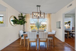 A dining area with a wooden table, four chairs, a chandelier, and a large plant.