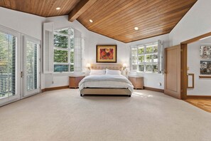 A bedroom with a large bed, two bedside lamps, a painting above the bed, and a view through the windows. - Spacious 5BR Vail retreat with river views and fireplace (Vail)