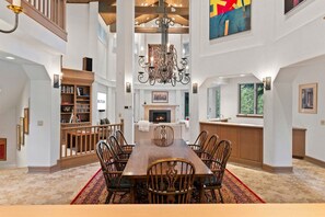 A spacious dining area with a large wooden table and chairs, a fireplace, and a bookshelf. - Spacious 5BR Vail retreat with river views and fireplace (Vail)