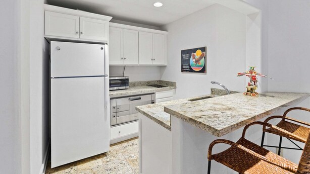 A compact kitchen with white cabinets, a built-in oven, a microwave, and a small island with a sink and bar stools. - Spacious 5BR Vail retreat with river views and fireplace (Vail)