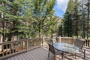 A deck with a glass table and chairs, surrounded by trees. - Spacious 5BR Vail retreat with river views and fireplace (Vail)