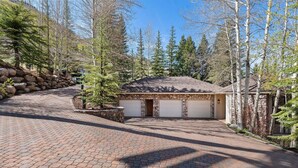 A stone building with two garage doors, surrounded by trees and a paved driveway. - Spacious 5BR Vail retreat with river views and fireplace (Vail)