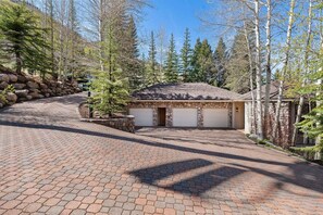 A stone building with two garage doors, surrounded by trees and a paved driveway. - Spacious 5BR Vail retreat with river views and fireplace (Vail)
