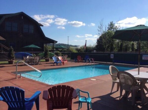 A swimming pool with lounge chairs and umbrellas, surrounded by a fence and trees.