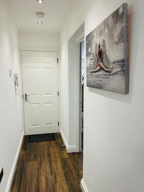 A hallway with a wooden floor, a white door, and a framed artwork on the wall. - 1 bed apt Close to Town Centre Train Station (Northampton)