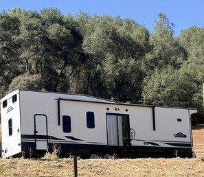 A single-story RV with a sliding door, a small window, and a logo on the side.