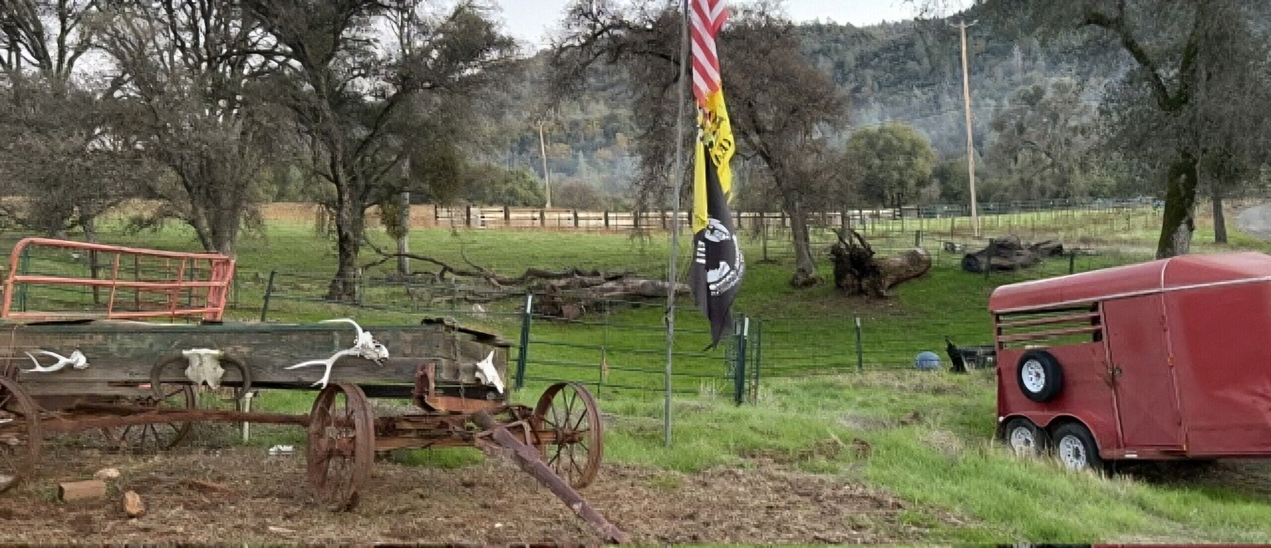 Paisagem rural com um trator antigo, um reboque vermelho e uma placa de cruzamento.