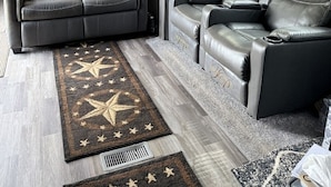 Compact interieur van een camper, met een bank, twee relaxfauteuils, een plafondventilator en een vloerkleed met dessin.