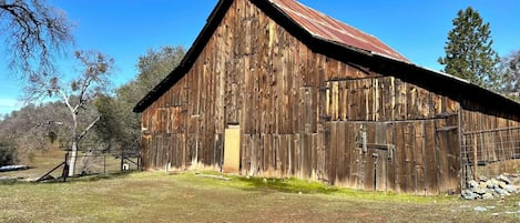 A large, rustic barn with a metal roof, surrounded by a grassy field and trees.