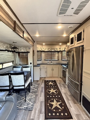 A compact kitchen with a dining area, a refrigerator, and a ceiling vent. - Destination Trailer on a 100 acre working Cattle Ranch with all comforts of home (Coulterville)