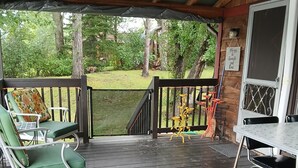 A covered outdoor seating area with a wooden deck, metal chairs, and a table.