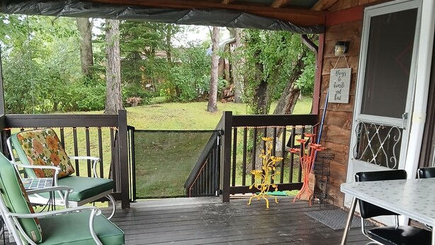 A covered outdoor seating area with a wooden deck, metal chairs, and a table.