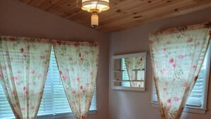 A bedroom with a bed, wooden ceiling, floral curtains, a dresser, and a mirror.