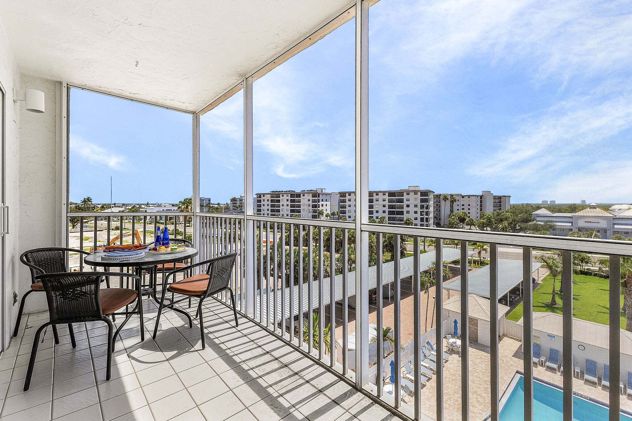 Uma varanda com mesa e cadeiras, uma piscina e vista para edifícios ao redor.