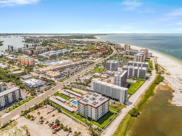 A coastal cityscape with high-rise buildings, a beach, and a marina. - Beachfront Dual Condo Escape with Pool, Gulf Views & Beach Access for Groups - Sand Caper - Roelens (Fort Myers Beach)