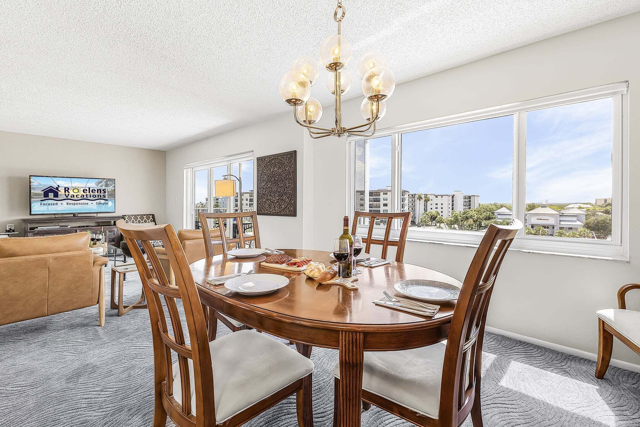 A dining area with a round table, chairs, a chandelier, and a television displaying a sign.