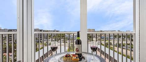 A balcony with a round table, two chairs, a bottle of wine, and a dessert tray.