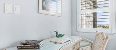 Una habitación con una mesa de vidrio, muebles de mimbre, un cuadro enmarcado y una ventana con persianas.