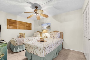 A bedroom with two beds, a ceiling fan, a wall-mounted wooden panel, and a painting. - Beachfront Dual Condo Escape with Pool, Gulf Views & Beach Access for Groups - Sand Caper - Roelens (Fort Myers Beach)