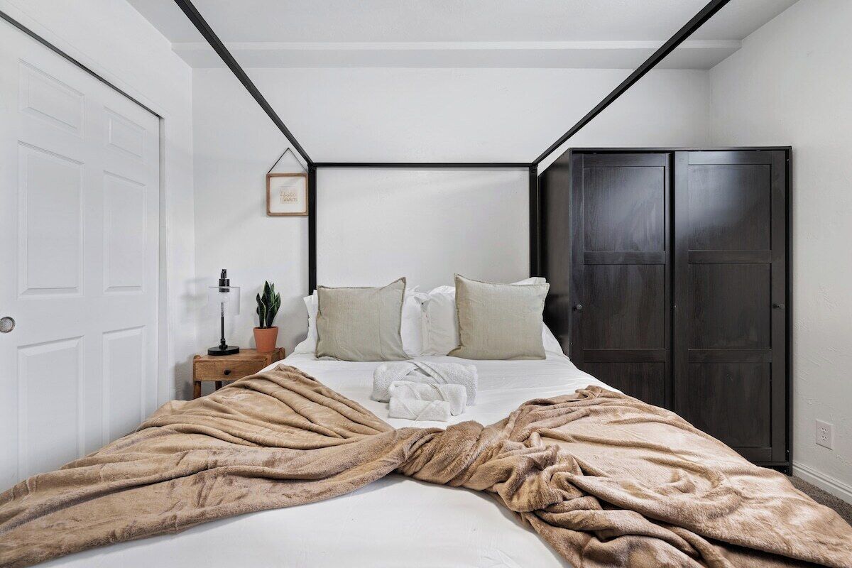 A bedroom with a bed, a bedside table with a lamp, a potted plant, and a wardrobe.