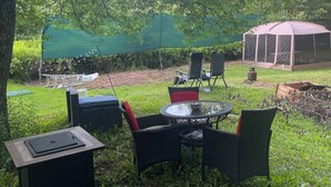 Un espacio al aire libre con sillas de mimbre y una mesa, rodeado de follaje y un dosel verde.