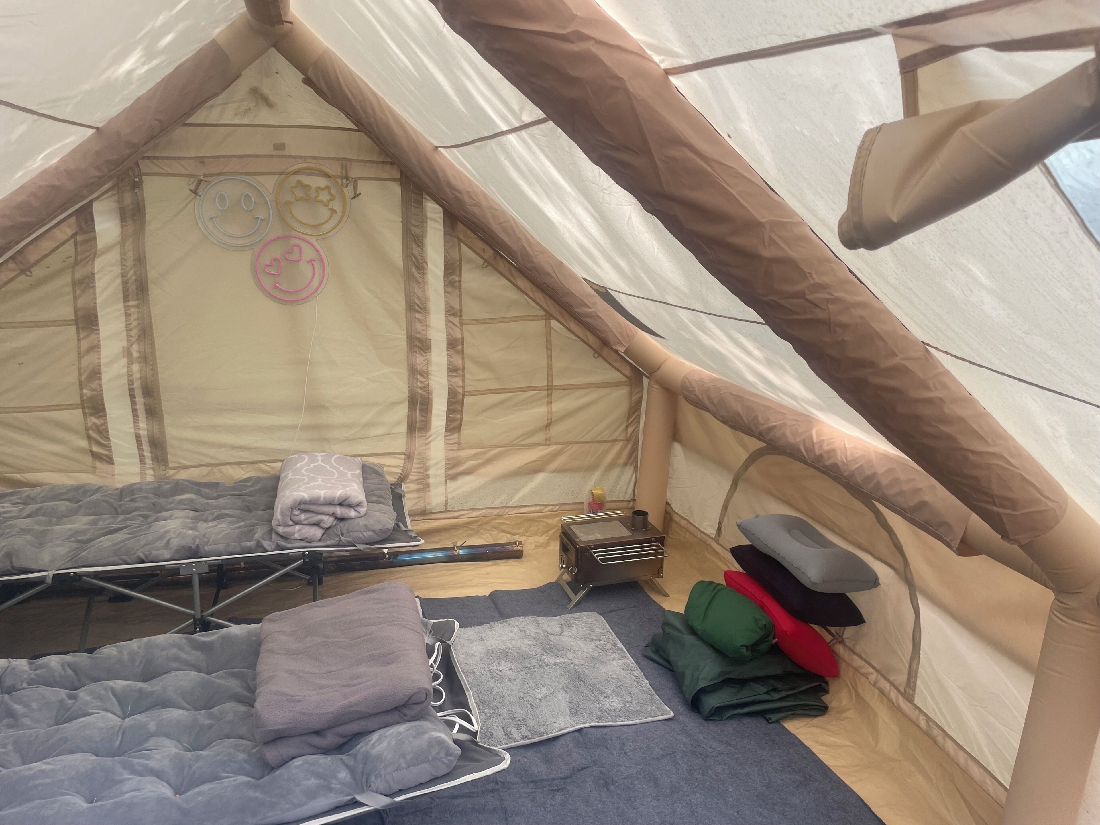 A tent with two sleeping areas, each with a mattress and pillows. There is a small heater and a folded mat on the floor.