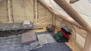 Tienda de campaña con dos zonas para dormir, cada una con colchón y almohadas. Hay un pequeño calentador y una colchoneta plegada en el suelo.