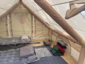 A tent with two sleeping areas, each with a mattress and pillows. There is a small heater and a folded mat on the floor.