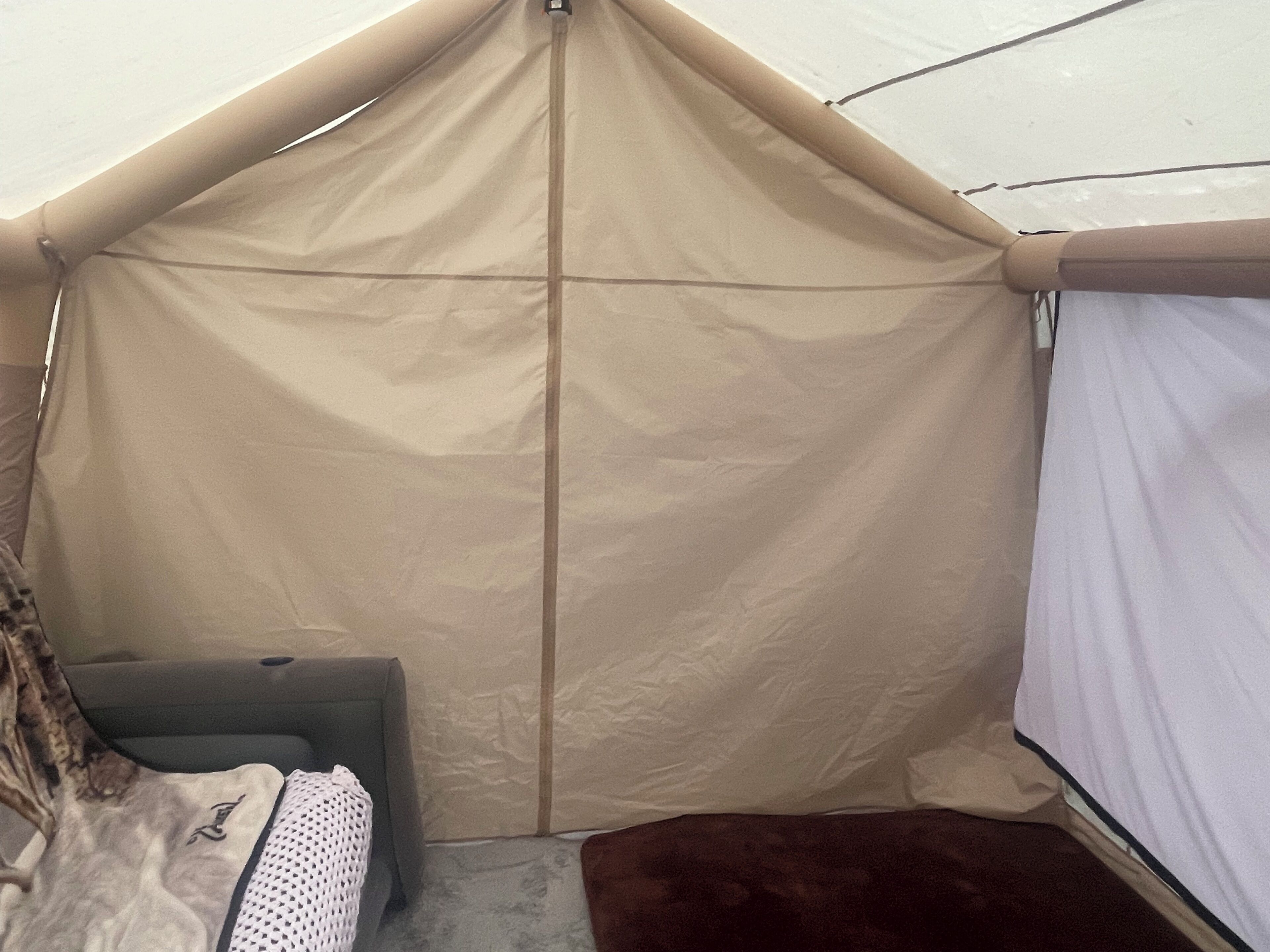 A tent with a zippered entrance, a cushioned bench, and a small table with a blanket.
