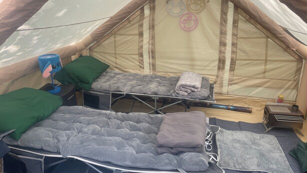 Una tienda de campaña con una cama, almohadas, una mesita y un calentador.