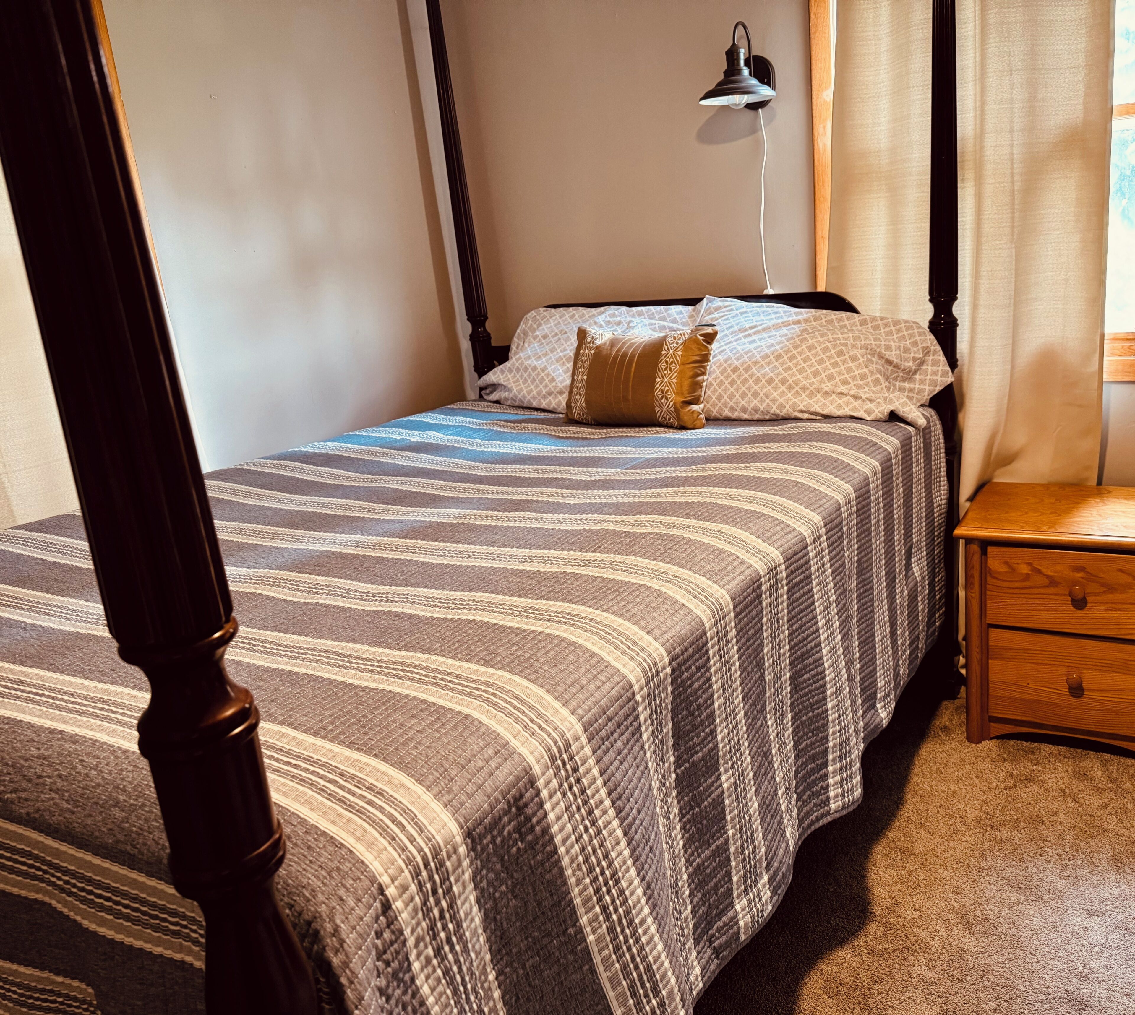 A bedroom with a four-poster bed, a bedside table, and a wall-mounted lamp.
