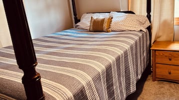 A bedroom with a four-poster bed, a bedside table, and a wall-mounted lamp.