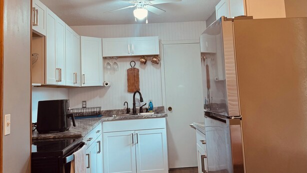 A kitchen with white cabinets, a black coffee maker, a stainless steel refrigerator, and a ceiling fan.