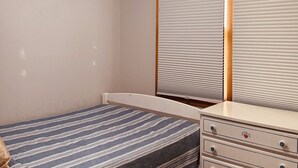 A bedroom with a bed, a dresser, a ceiling fan, and a window with blinds.