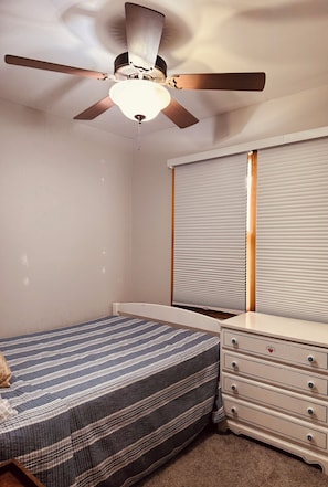 A bedroom with a bed, a dresser, a ceiling fan, and a window with blinds.