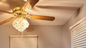 A dining area with a wooden table and bench seating, a ceiling fan, and two windows with blinds.