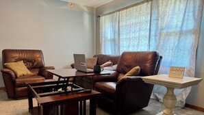 A living room with leather sofas, a wooden coffee table, a laptop, and a sign on a pedestal table.