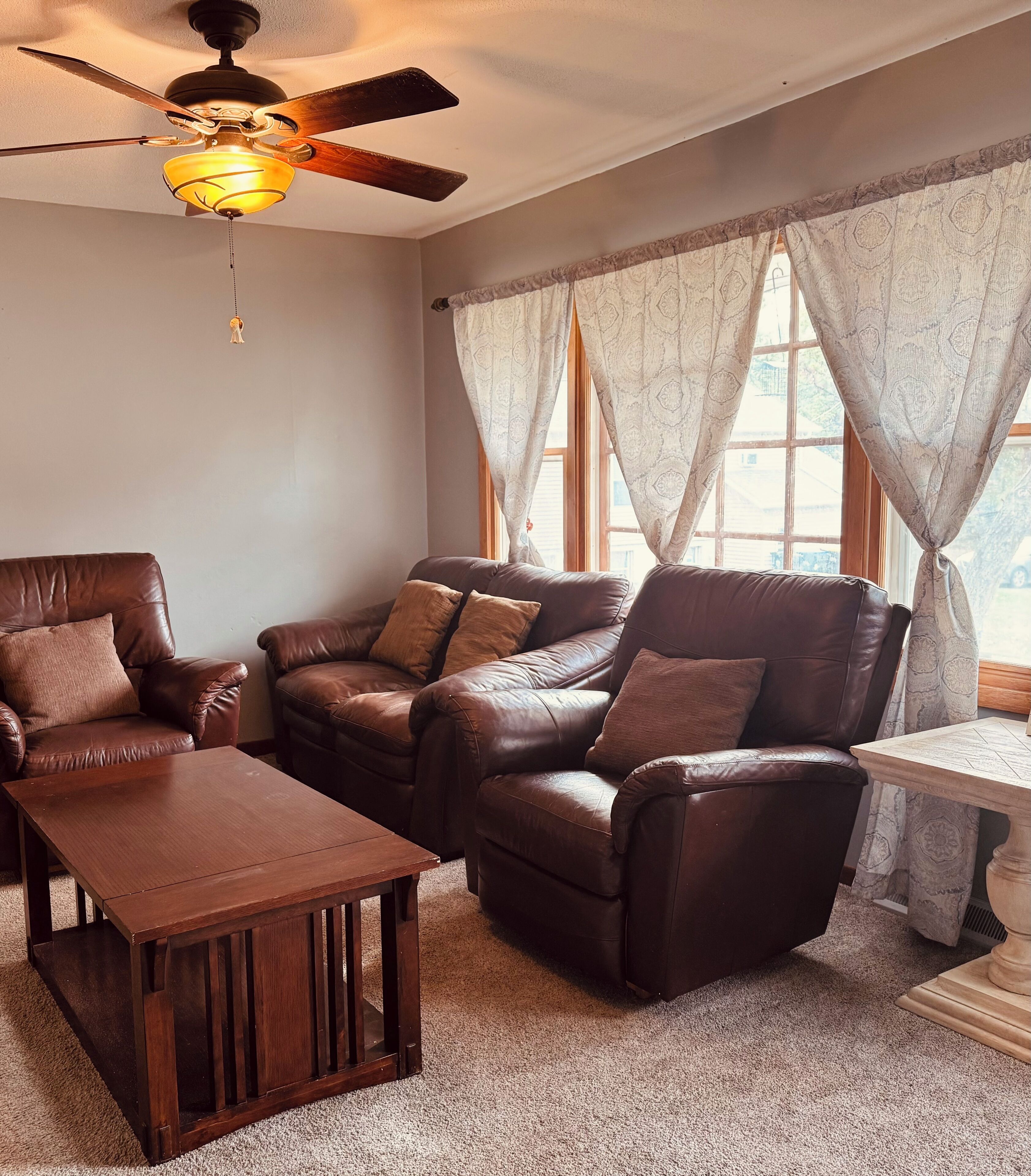 A living room with a ceiling fan, a wooden coffee table, and leather sofas with cushions.
