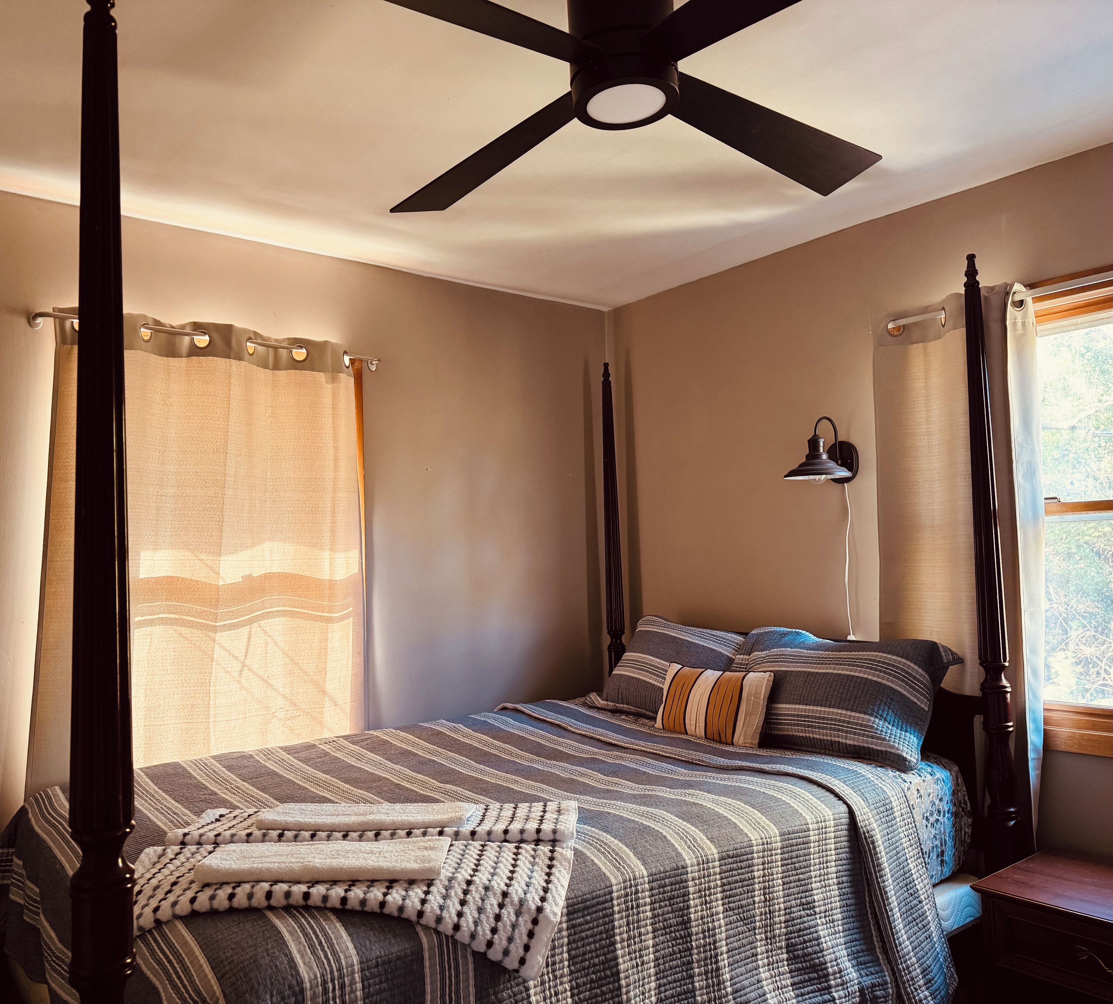 A bedroom with a bed, a ceiling fan, a window with curtains, and a bedside lamp.