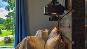 Une pièce avec un lit adossé à un mur, une fenêtre avec des rideaux et un luminaire fixé au mur.