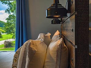 Ein Zimmer mit einem Bett an der Wand, einem Fenster mit Vorhängen und einer Wandleuchte.